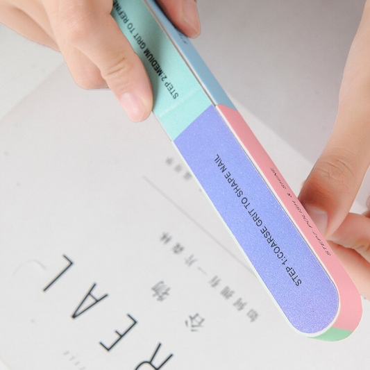 Nail file with gradient colors held by a hand on a blurred background
